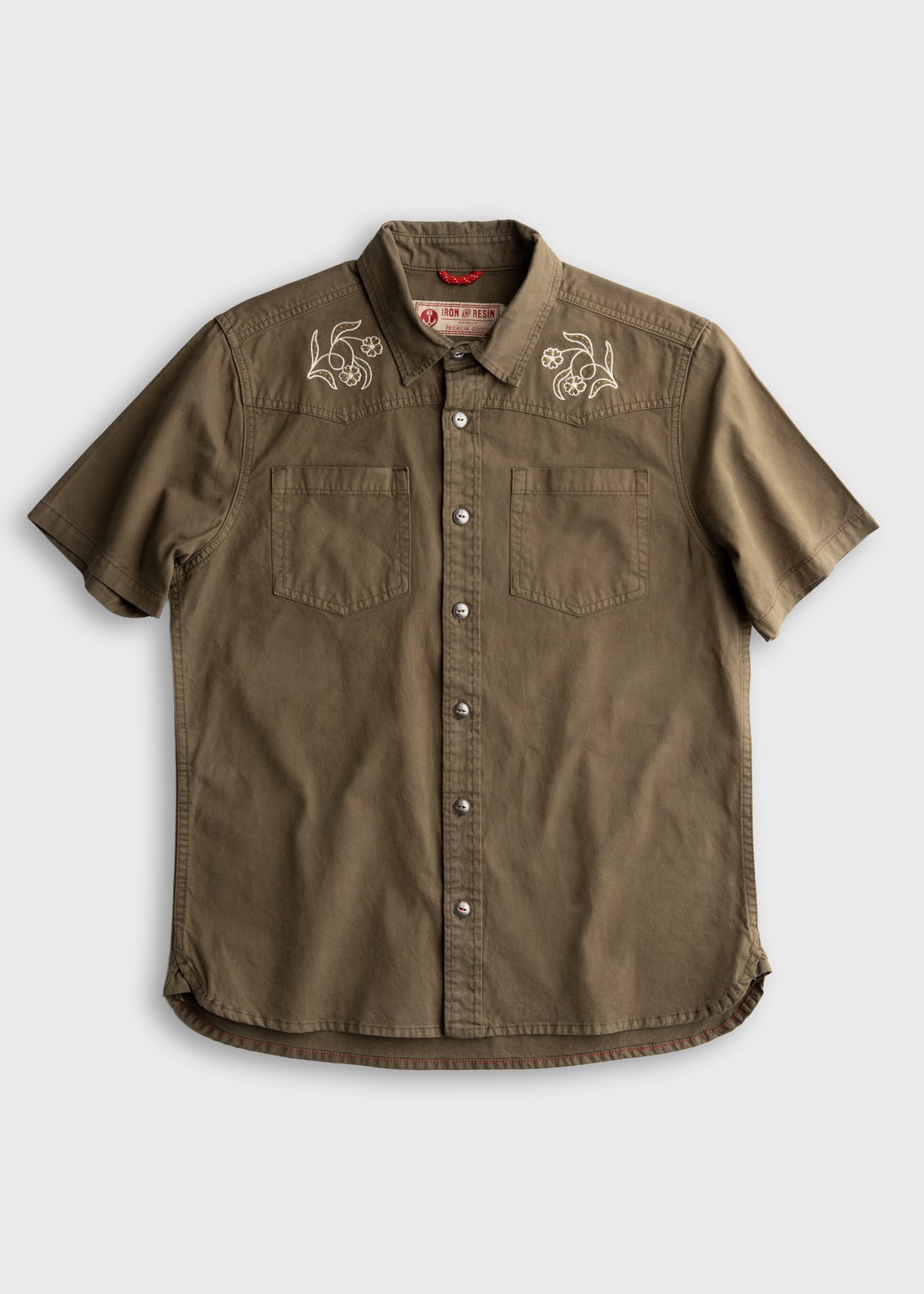 Olive green short-sleeve shirt with floral embroidery on shoulders, button front, and two chest pockets on a plain background.