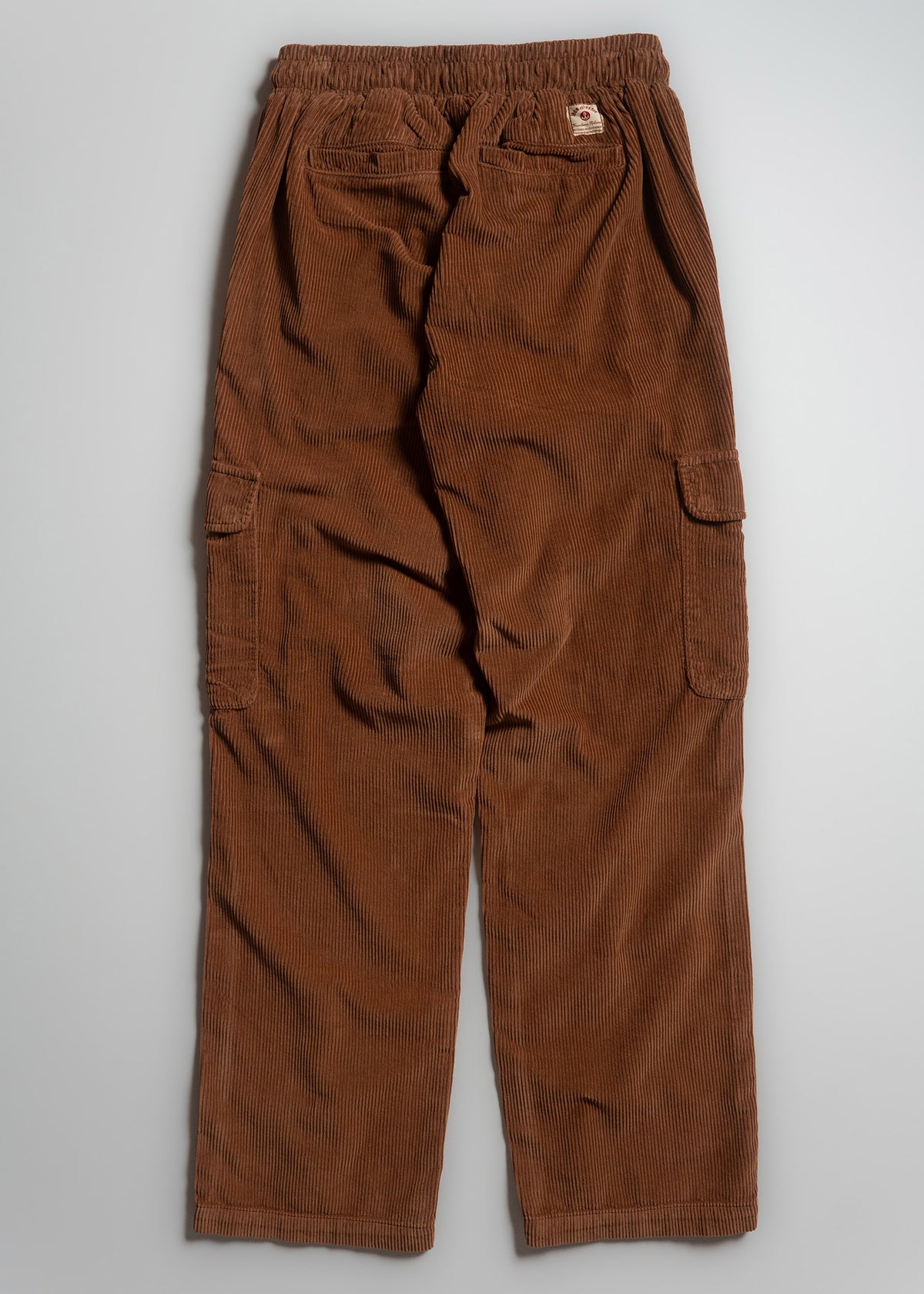 Brown corduroy cargo pants with elastic waistband and multiple pockets, laid flat on a light gray background.