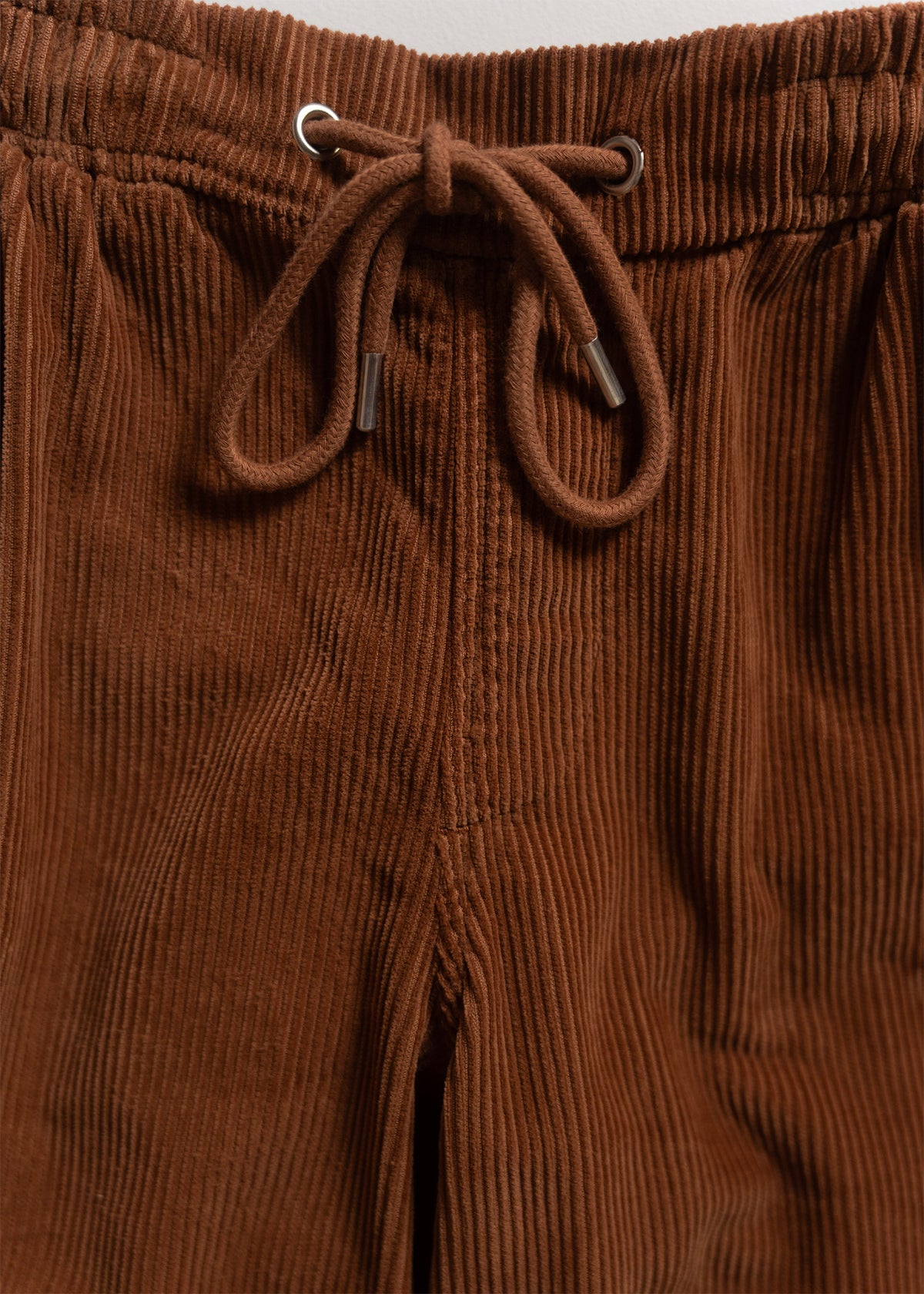 Close-up of brown corduroy pants with an elastic waistband and drawstring, showcasing the fabric's texture and detail.