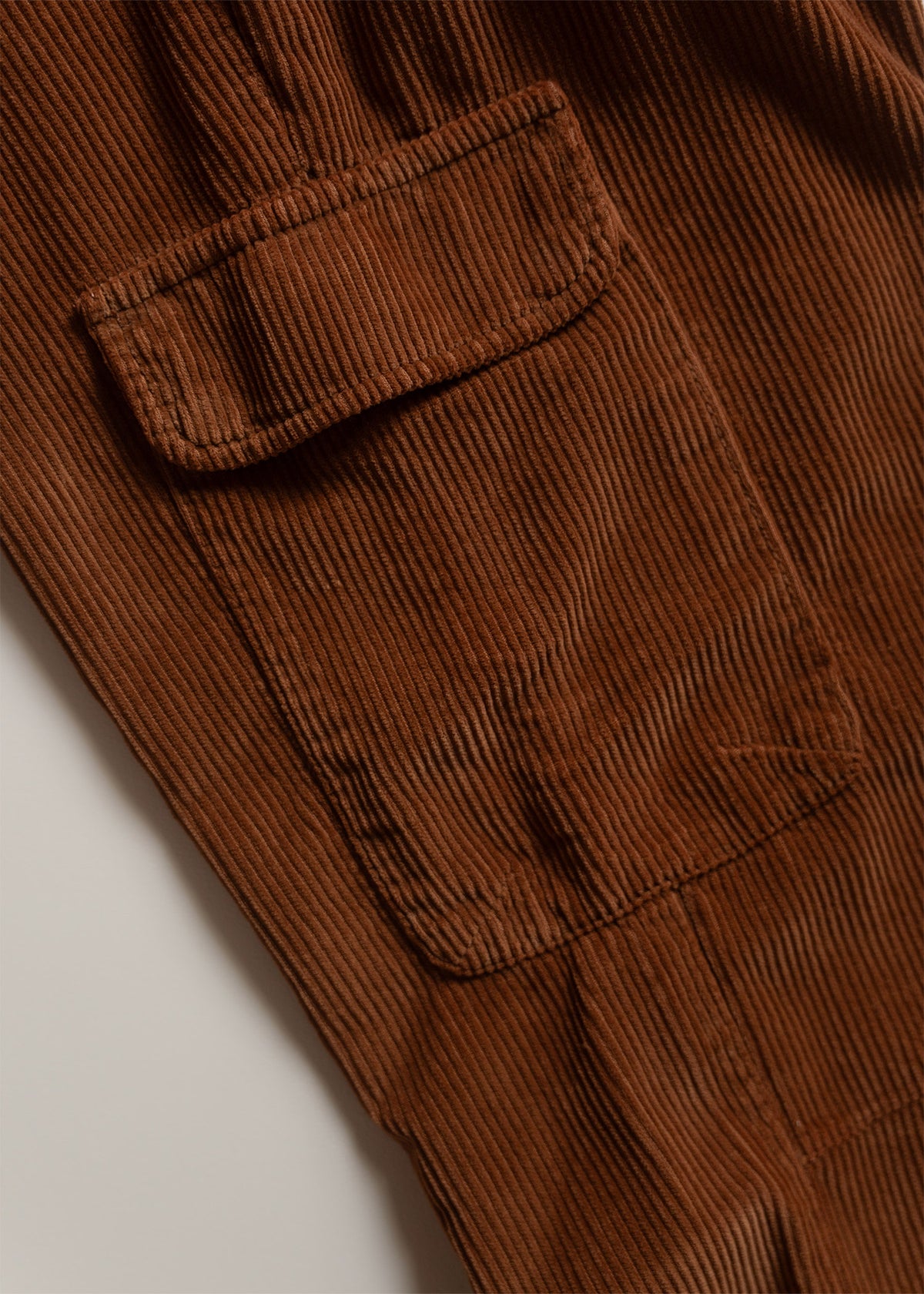 Close-up of brown corduroy fabric with a flap pocket, showcasing its textured pattern and rich color in soft lighting.
