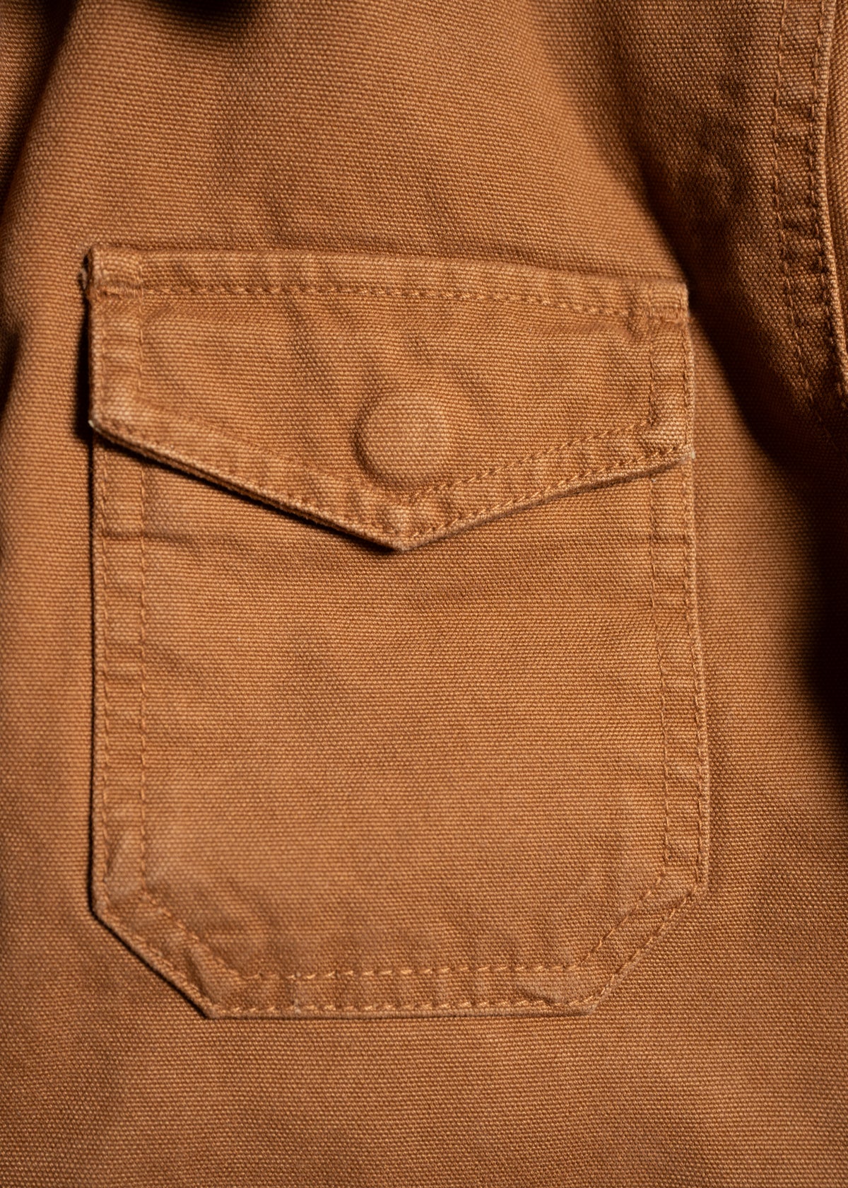 Close-up of a brown fabric shirt pocket with a buttoned flap, highlighting the texture and stitching details.