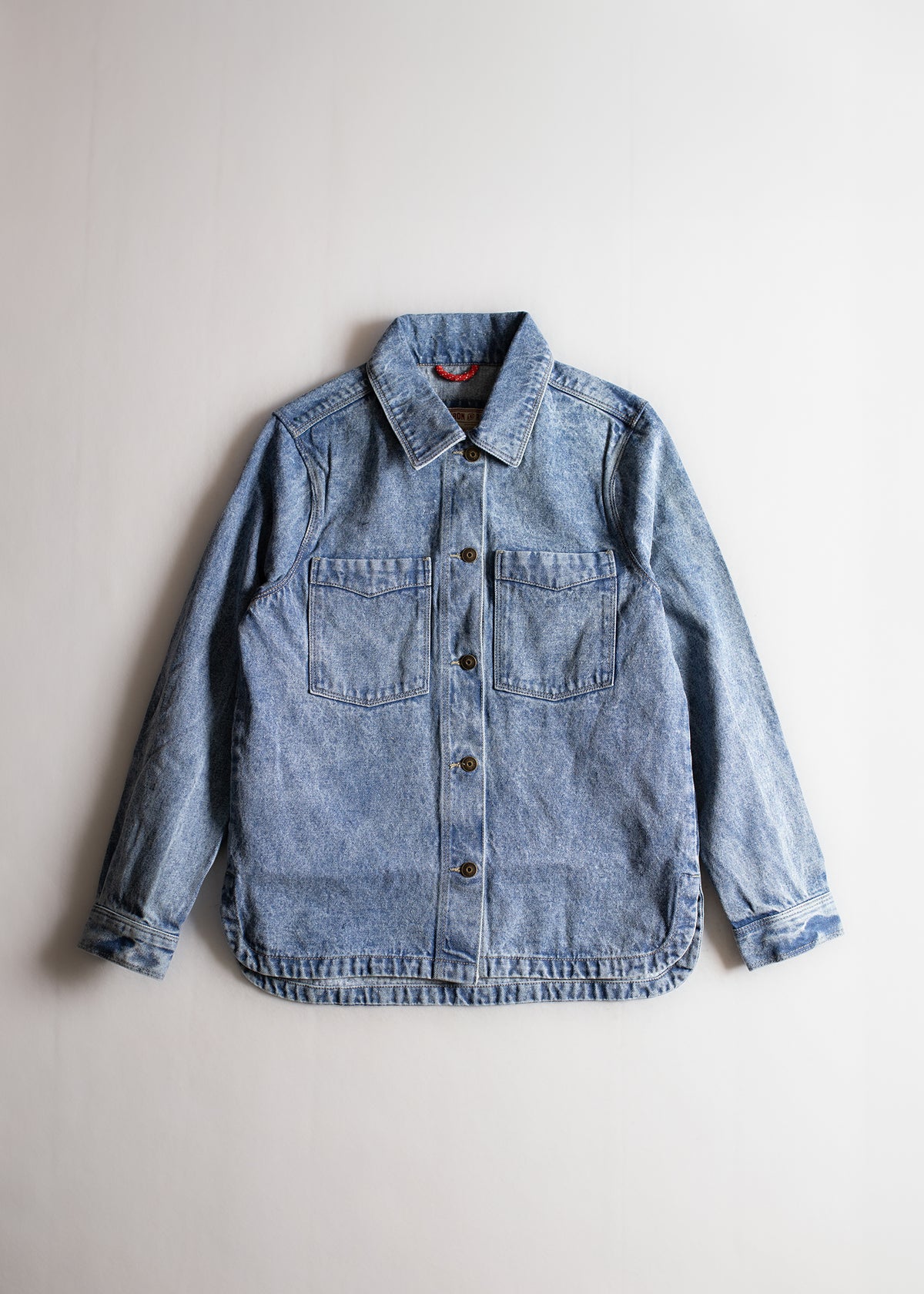 Light blue denim jacket with button closure and two chest pockets, displayed on a plain white background.