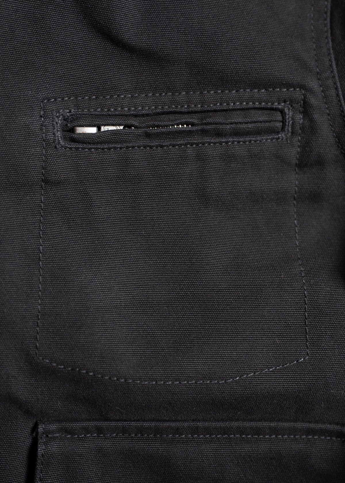 Close-up of a black fabric jacket pocket with a visible zipper, showcasing detailed stitching and texture.