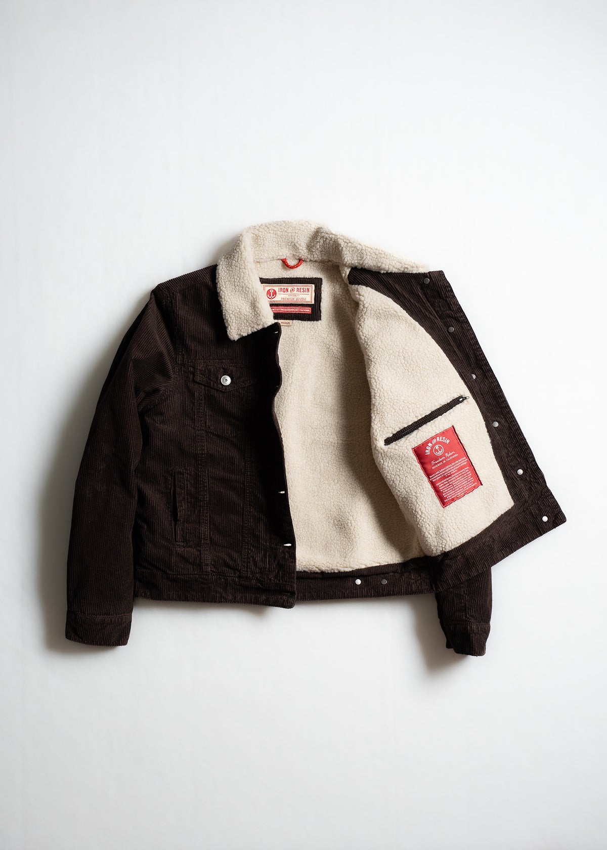 Brown corduroy jacket with a white fleece lining, open to reveal a red label inside, displayed on a plain white background.