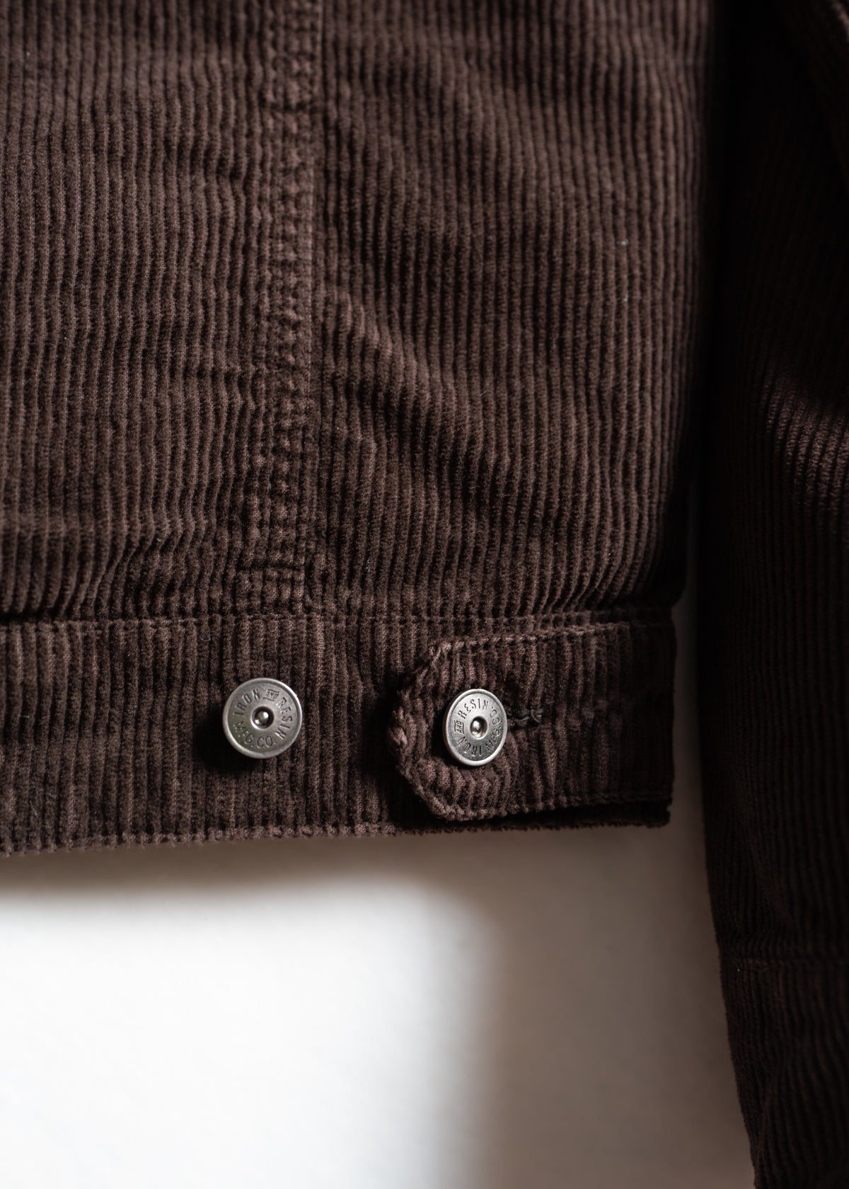 Close-up of brown corduroy fabric with two metallic buttons, highlighting texture and detail in natural light.