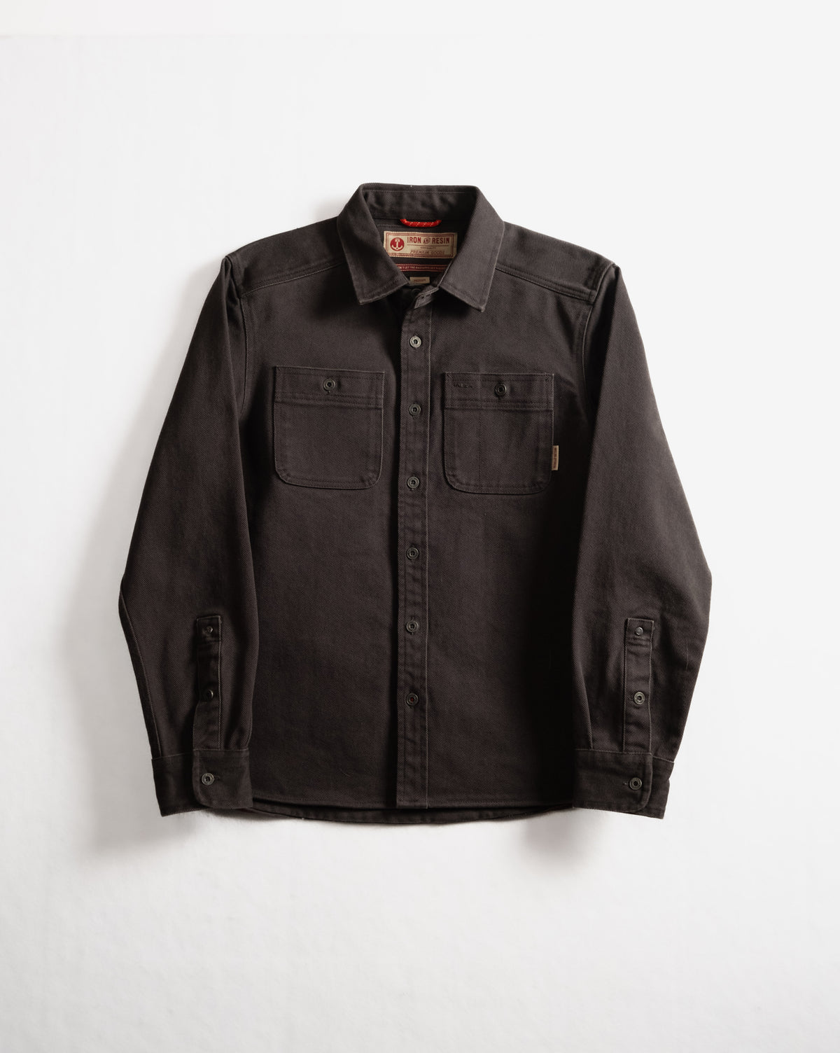 Dark button-up shirt with two chest pockets, displayed on a white background. The shirt has a classic collar and long sleeves.