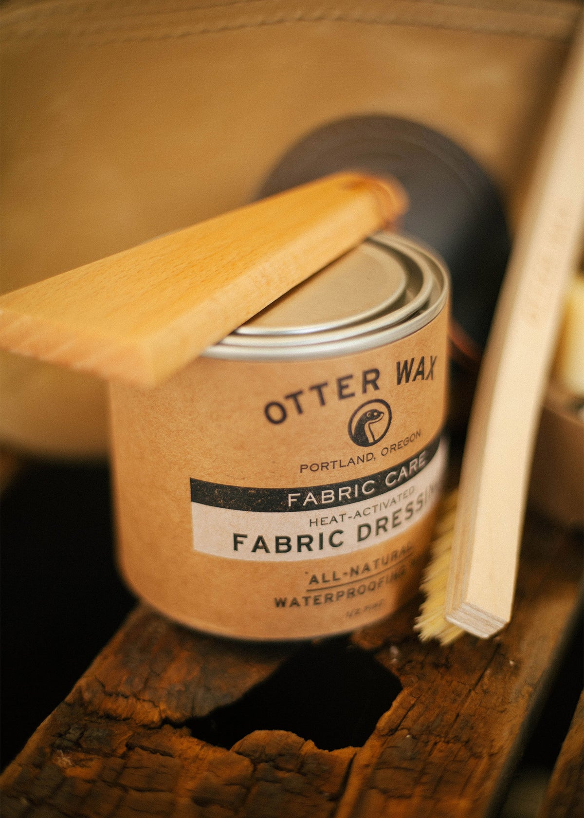 Otter Wax Fabric Dressing tin with wooden applicator on rustic surface, highlighting natural waterproofing and fabric care.